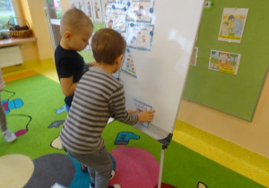 Dwóch chłopców zawiesza na tablicy zasady z Kodeksu dobrych relacji.